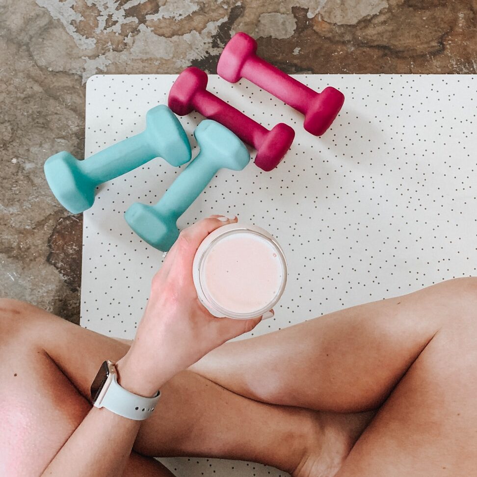 person holding white liquid filled cup above two pairs of dumbbells